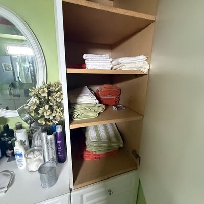 Open bathroom storage cabinet filled with stacks of folded towels and washcloths, alongside a vanity counter with various toiletries.