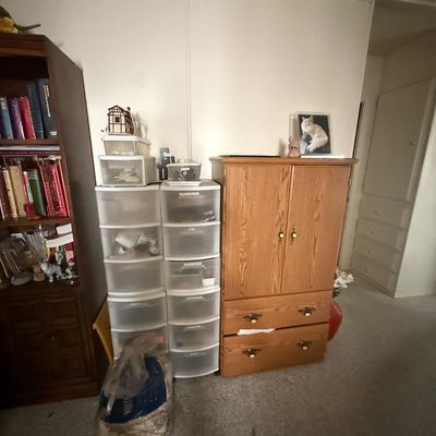 Traditional oak armoire featuring two lower drawers alongside stackable plastic storage drawers and a dark wood bookcase.