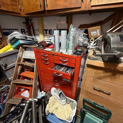 Red vintage Cornwell metal tool chest filled with various hand tools, positioned in a workshop alongside a heavy-duty bench vise,...