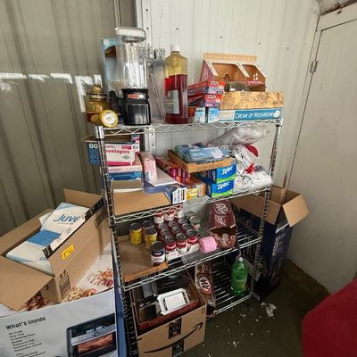 Four-tier wire shelving unit filled with household goods, office supplies, canned foods, and small appliances.
