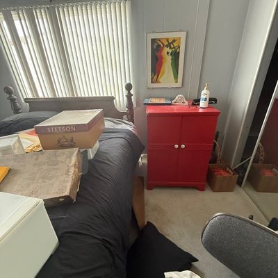 Bedroom featuring a wooden four-poster bed frame, a bright red two-door cabinet, a vintage Stetson hat box, framed wall art, and various...