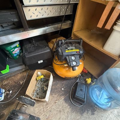 Bostitch 6-gallon pancake air compressor with dual pressure gauges, shown alongside workshop tools, hardware, and shelving.