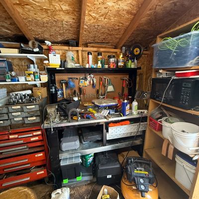 Workshop shed filled with tools, featuring a Bostitch pancake air compressor, a heavy-duty metal workbench with attached pegboard, red...