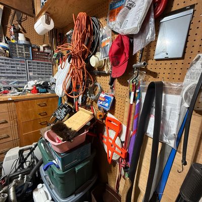 Workshop wall pegboard filled with assorted hand tools, extension cords, hardware supplies, and storage bins.