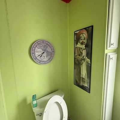 Round vintage-style wall clock with world map face alongside framed vertical wall art in a lime green bathroom.