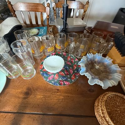 Collection of vintage glassware on a wooden table, including Dad's Root Beer mugs, drinking glasses, a ruffle-rimmed opalescent...