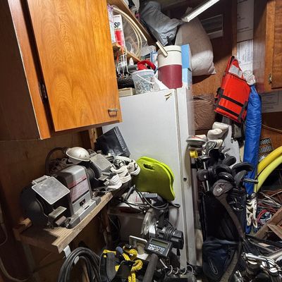 Cluttered workshop and storage area featuring bench grinders, power tools, a White's MXT metal detector, golf clubs, a life jacket,...