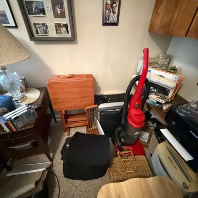 A collection of household goods, including a red Dirt Devil upright vacuum, wooden folding TV tray tables, framed family photo collages,...
