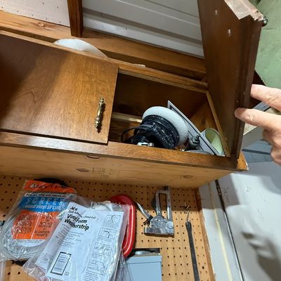 Wall-mounted wooden storage cabinet with a pull-up door, filled with miscellaneous tools and workshop supplies.