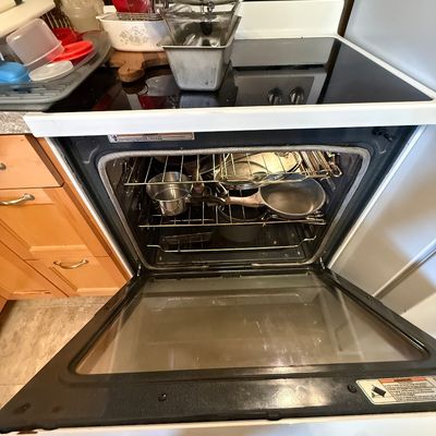 White electric range with smooth cooktop, filled with stored cookware both inside the oven and on top.