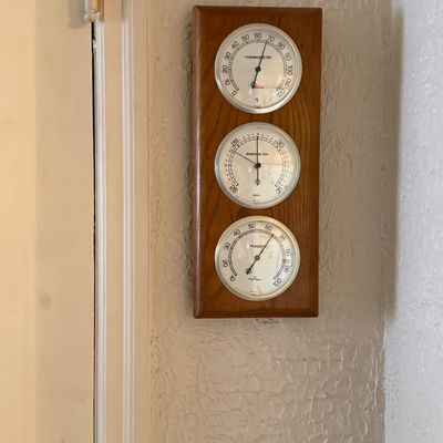 Wall-mounted weather station with thermometer, barometer, and hygrometer gauges set in a vertical wood plaque.