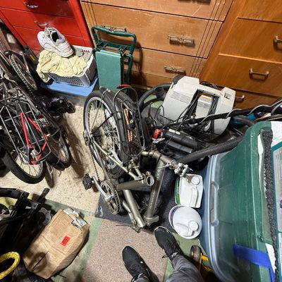 Dahon Adventurer folding bicycle resting in a crowded storage space alongside various household items and furniture.