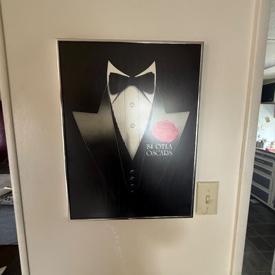 Framed '84 OTLA Oscars poster featuring a tuxedo graphic with a pink carnation, presented in a simple metal frame.