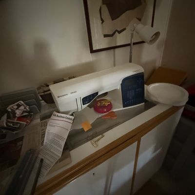 Husqvarna Viking computerised sewing machine resting on a wooden cabinet, accompanied by sewing accessories and paper instruction sheets.