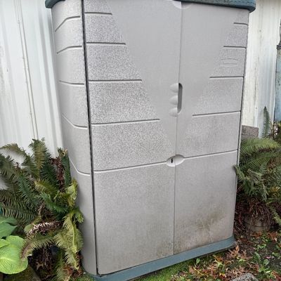 Rubbermaid outdoor resin storage shed in light gray with a dark green roof and trim, showing light weathering from outdoor placement.