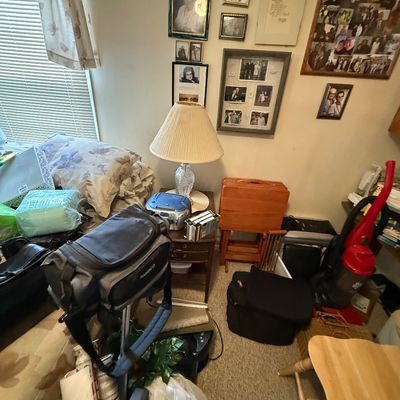 Assorted household items, including a portable boombox, framed family photos, luggage, a red upright vacuum cleaner, and a set of wooden...