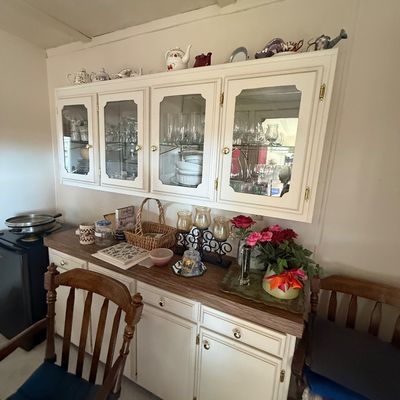 Off-white painted china cabinet hutches and buffet set, featuring glass-front upper doors filled with glassware and a wooden countertop.