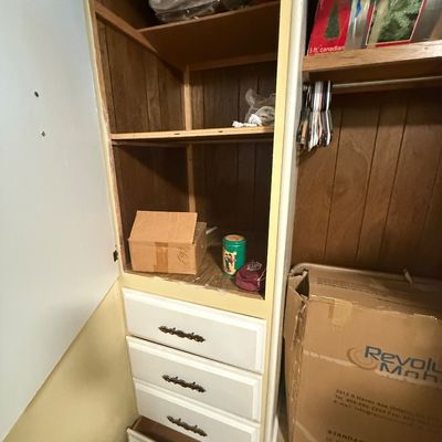 Built-in closet cabinet with white painted drawer fronts and wood-paneled shelving sections.