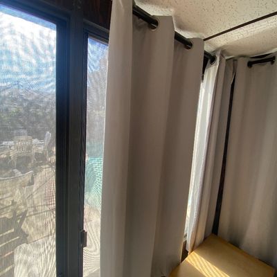 Sale Photo Thumbnail #190: Set of modern off-white grommet-top blackout curtain panels hanging on a dark metal rod alongside sliding glass doors.