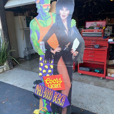 Sale Photo Thumbnail #103: Vintage Coors Light Halloween cardboard standee featuring Elvira, Mistress of the Dark, and a Frankenstein's monster figure, labeled 'Mali-BOO Beach'.
