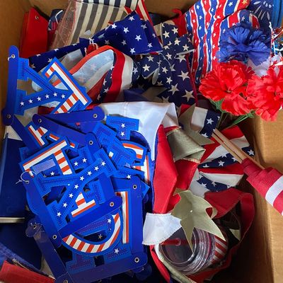 Sale Photo Thumbnail #123: Cardboard box filled with patriotic 4th of July decorations, including flags, banners, oven mitts, and artificial flowers.