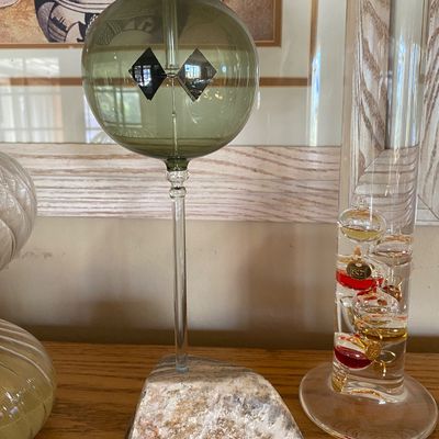 Sale Photo Thumbnail #95: Glass radiometer mounted on a natural stone base, shown alongside a glass Galileo thermometer.