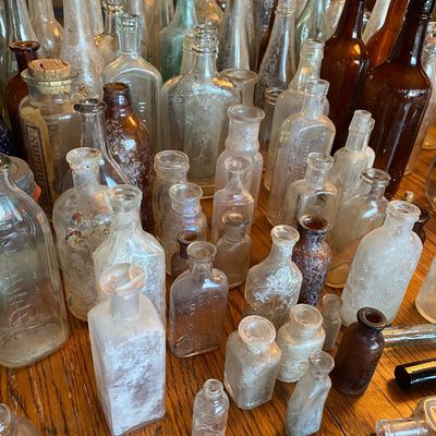 Sale Photo Thumbnail #51: Large collection of antique glass bottles in various sizes, shapes, and colors, including clear, amber, and light blue apothecary and beverage bottles.