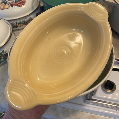 Sale Photo Thumbnail #45: Vintage yellow Fiestaware oval baker in good condition, displayed with other ceramic cookware in the background.