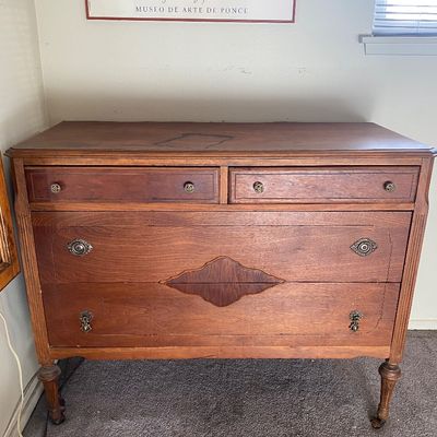 Sale Photo Thumbnail #63: Vintage wood dresser featuring decorative central wood appliqués, fluted corner details, and metal pull hardware, resting on turned legs.