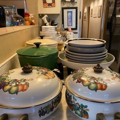 Sale Photo Thumbnail #2: Collection of kitchenware featuring a pair of vintage enamel-on-steel oval Dutch ovens with fruit motif, alongside cast iron cookware and stacked dishware.