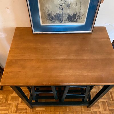 Sale Photo Thumbnail #41: Wooden kitchen island or high-top table with a natural wood top and dark painted base, shown with two matching stools stored underneath.