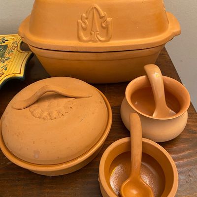 Sale Photo Thumbnail #66: Collection of unglazed terracotta cookware and serving pieces, including a Romertopf-style clay roaster with leaf motifs, a covered dish, and two small pots with matching spoons.
