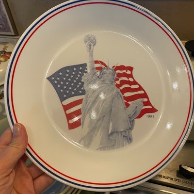 Sale Photo Thumbnail #46: Corelle Commemorative 1991 patriotic ceramic plate featuring the Statue of Liberty against an American flag graphic with red and blue rim trim.