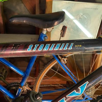 Sale Photo Thumbnail #116: Vintage Stonehill MTB mountain bike featuring a blue frame with purple-to-black gradient top tube branding, black saddle, and mounted water bottle.