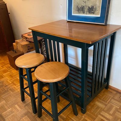 Sale Photo Thumbnail #62: Two-tone kitchen island table featuring a natural wood top, dark green frame with slatted sides, lower storage shelf, and a pair of matching backless barstools.