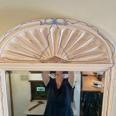 Sale Photo Thumbnail #40: Vintage arched wall mirror featuring a whitewashed wooden frame with hand-painted ribbon details and a fluted crown.