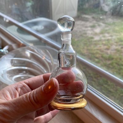 Sale Photo Thumbnail #93: Small clear glass perfume decanter with a matching glass stopper and gold-trimmed base.
