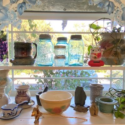 Sale Photo Thumbnail #94: Collection of decorative glassware and ceramics displayed on window shelves, including vintage aqua blue Ball Mason jars, ceramic vases, a ceramic mug with a cat motif, and small potted plants.