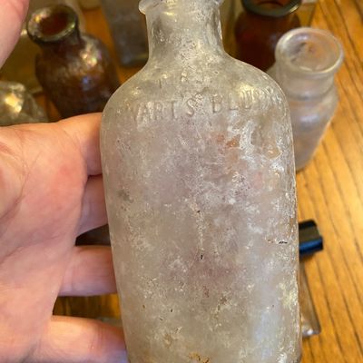 Sale Photo Thumbnail #54: Antique clear glass medicine bottle with embossed text 'STEWART'S BLUING', featuring heavy surface patina and weathering.