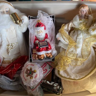 Sale Photo Thumbnail #118: Assortment of vintage Christmas decorations stored in a tub, featuring a plush Santa figure with brass bell, a boxed blown-glass Santa ornament, and an elegant angel tree topper in a gold and white dress.