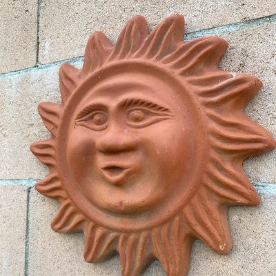 Sale Photo Thumbnail #180: Terracotta sun face wall plaque with sculpted details, mounted on a stone block wall.