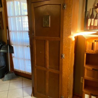 Sale Photo Thumbnail #70: Tall antique wooden corner armoire or storage cabinet featuring decorative brass hinges and a carved top molding.