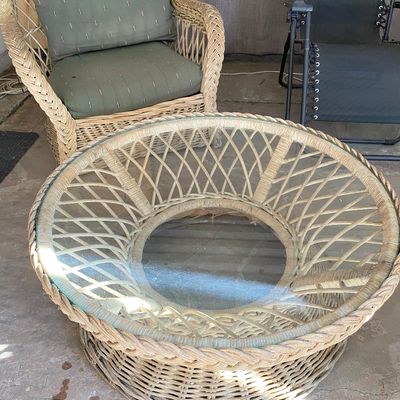 Sale Photo Thumbnail #56: Round woven wicker coffee table with a glass insert top, accompanied by a matching wicker armchair with green cushions.