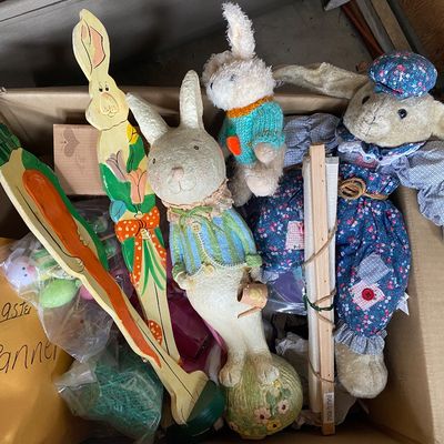 Sale Photo Thumbnail #124: Collection of vintage Easter decorations inside a cardboard box, including painted wooden bunny stakes, plush rabbit dolls, and resin figures.