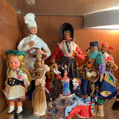 Sale Photo Thumbnail #73: Collection of vintage international folk dolls and figurines displayed in a wooden cabinet shelf.