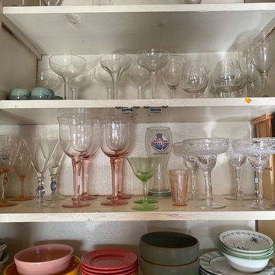 Sale Photo Thumbnail #12: A cupboard filled with various glassware and ceramic dishware, including margarita glasses, stemmed pink and clear wine glasses, green glass, and colorful stacked bowls.