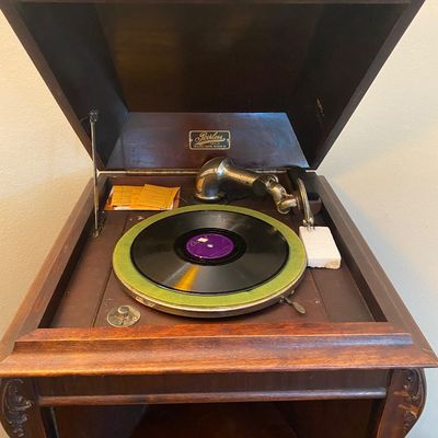Sale Photo Thumbnail #60: Antique Peerless brand floor-standing phonograph featuring a hinged wooden cabinet, green felt turntable mat, and original tone arm.