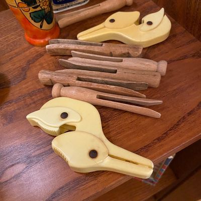 Sale Photo Thumbnail #164: Collection of vintage wooden clothespins alongside bird-shaped plastic utility clips, displayed on a wooden shelf next to small collectible tins.