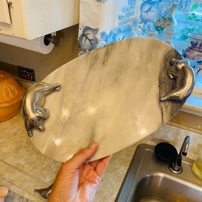 Sale Photo Thumbnail #50: Oval white and gray marble serving tray featuring cast metal pig-shaped handles on both sides.