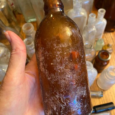 Sale Photo Thumbnail #55: Vintage amber glass bottle with visible surface patina, held against a collection of antique glass bottles.